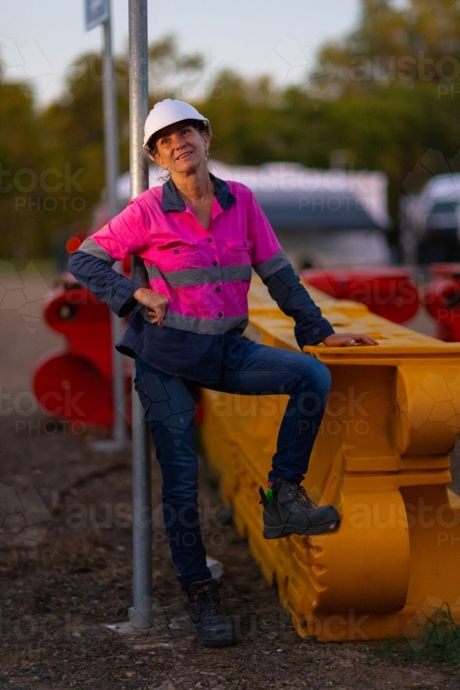 mature woman standing outdoors on industrial site wearing workwear and a hard hat. - Australian Stock Image