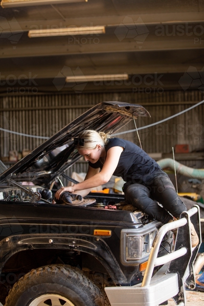 Mechanic leaning under hood of 4wd car fixing the engine - Australian Stock Image