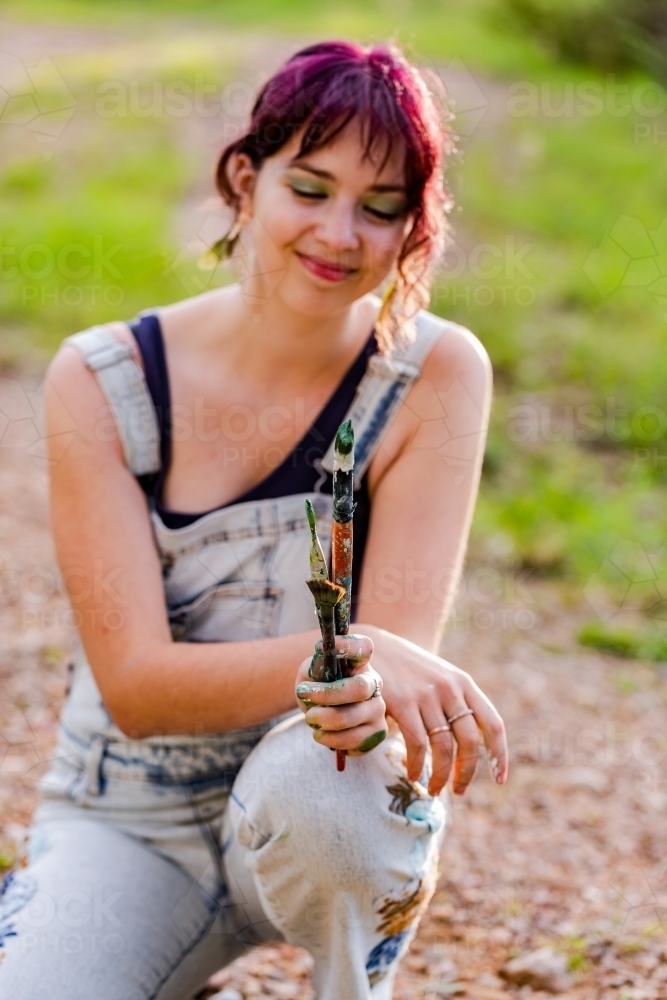 Messy paint brushes in hand of young artist - Australian Stock Image