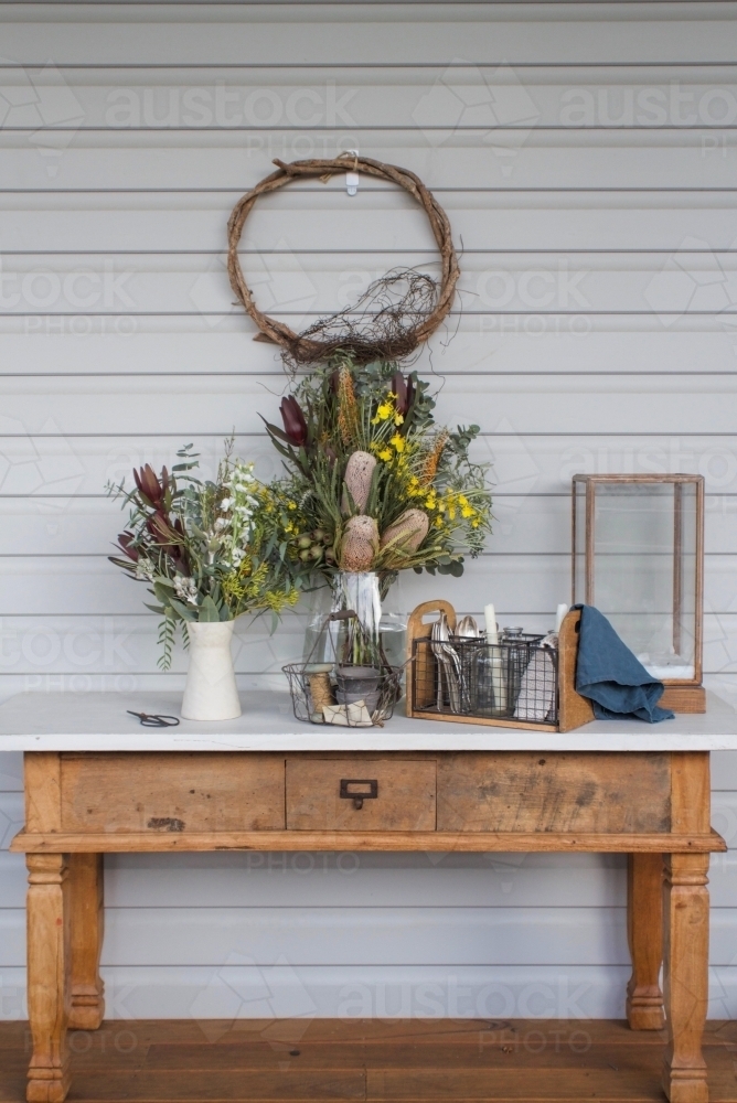 Antique wooden table with wreath, vases of flowers and wire baskets - Australian Stock Image