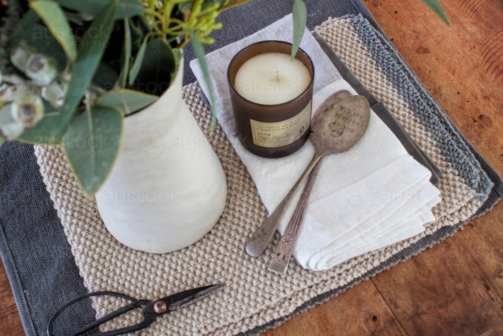 Top down view of wooden table with vase of eucalyptus, old fashioned scissors, candle and spoons - Australian Stock Image