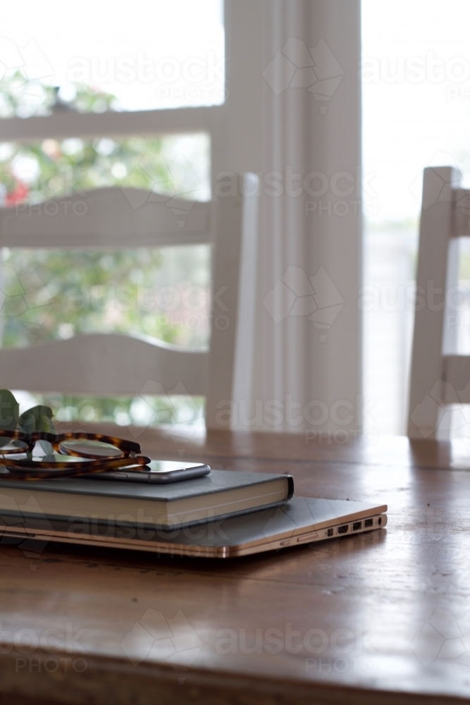 Dining table with laptop, book, phone and glasses - Australian Stock Image