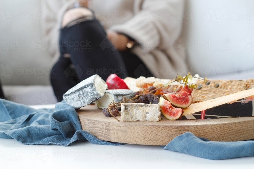 Close up of cheese platter with blurred seated woman in background - Australian Stock Image