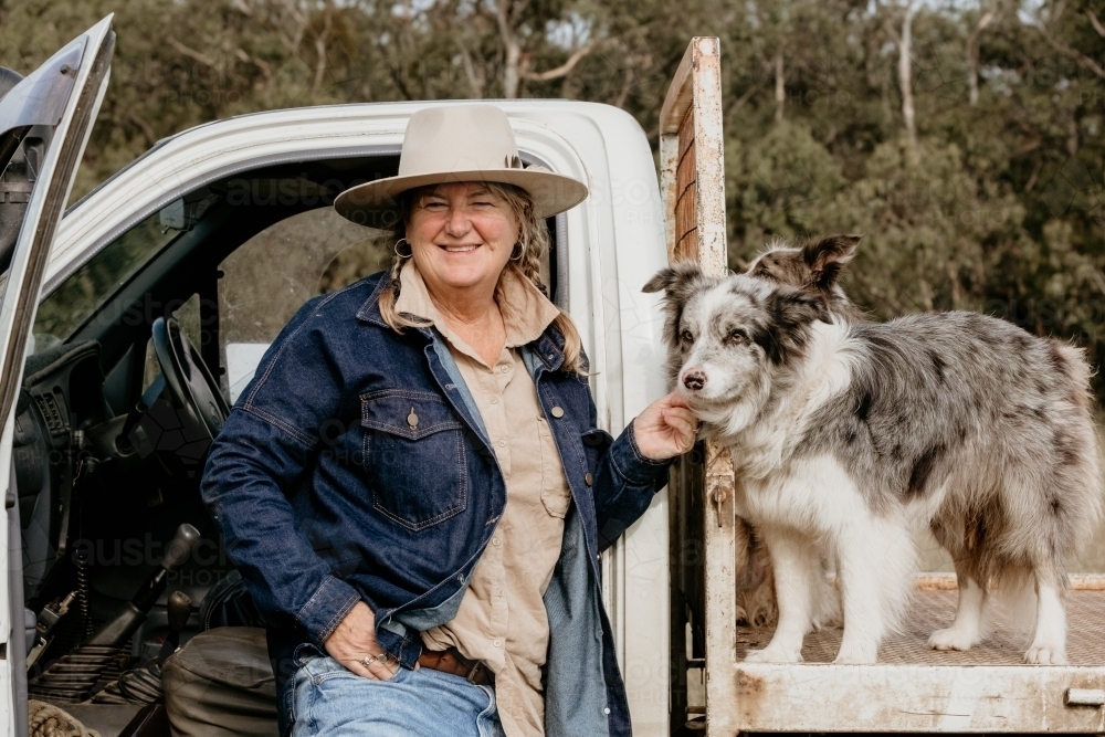 Mid fifties woman smiles and pats dog on ute. - Australian Stock Image