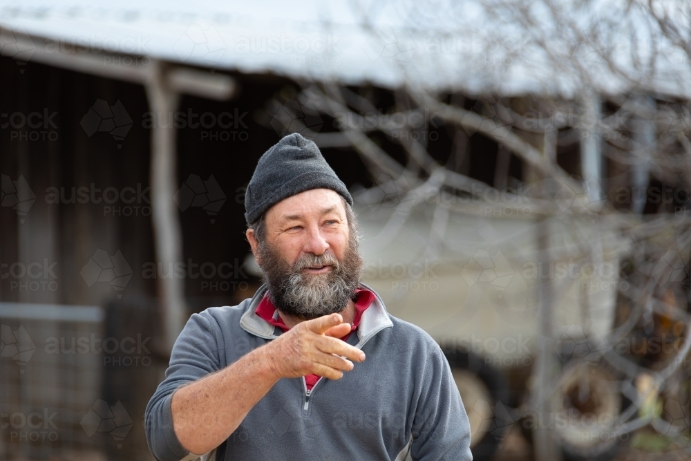 Middle aged country bloke with a bushy beard wearing a beanie pointing at something - Australian Stock Image