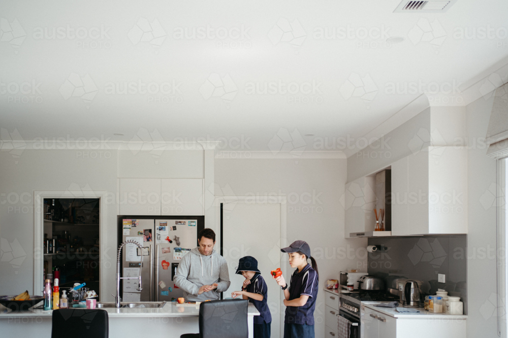 Middle-aged dad cutting fruit on the kitchen counter with his kids getting school snacks ready - Australian Stock Image