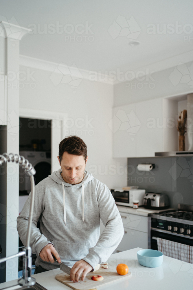 Middle-aged guy cutting fruits on the kitchen counter. - Australian Stock Image