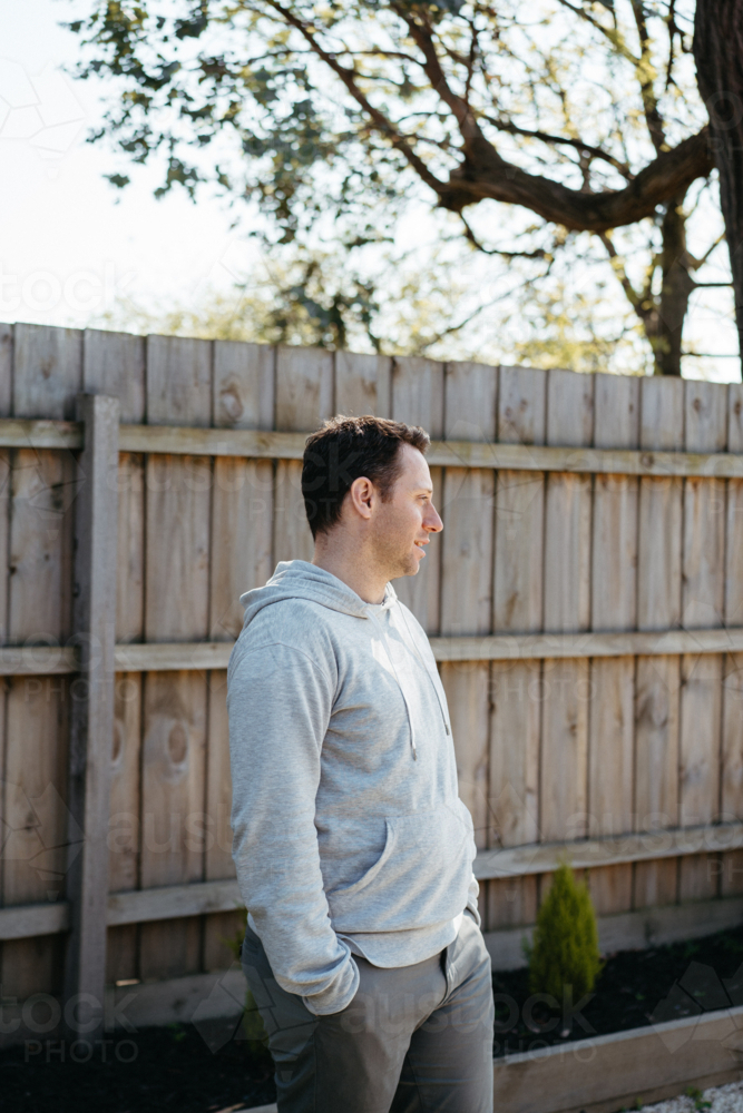 Middle-aged man standing in front of a wooden fence in the yard - Australian Stock Image