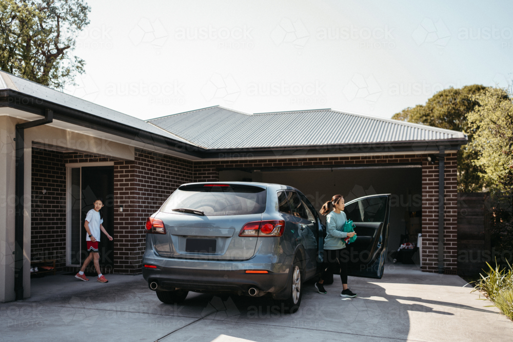 Middle-aged woman getting out of the car in the driveway of home - Australian Stock Image