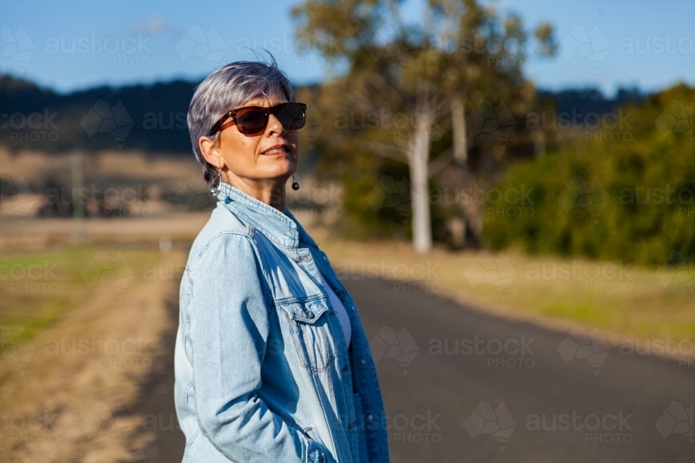 Middle aged woman walking down a rural road for exercise - Australian Stock Image