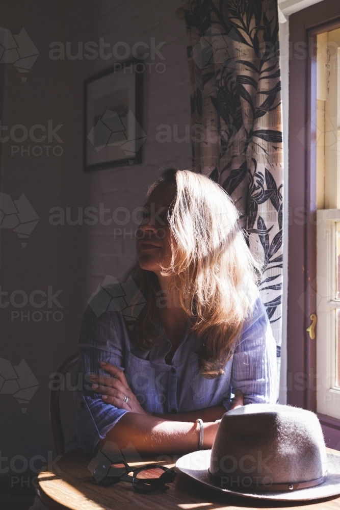 Middle-aged woman with brown hair sitting near the window. - Australian Stock Image