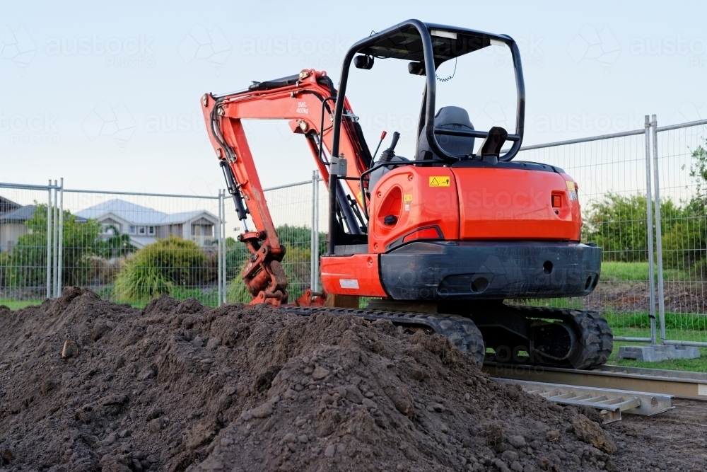 Mini digger standing idle at a construction site - red excavator - Australian Stock Image