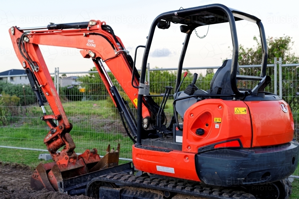 Mini digger standing idle at a construction site - red excavator - Australian Stock Image