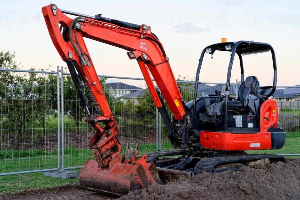 Mini digger standing idle at a construction site - red excavator - Australian Stock Image