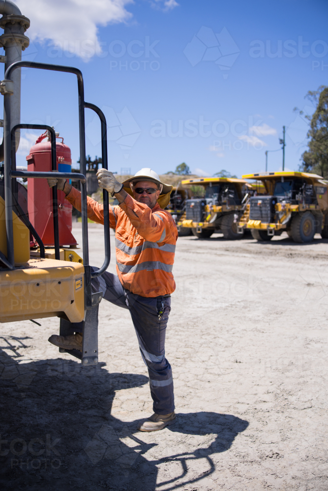 Mining operator man holding on the handrails while climbing up the dump truck - Australian Stock Image