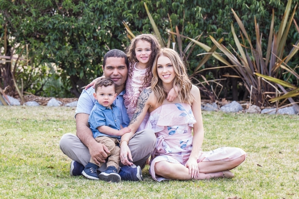 Mixed race aboriginal and caucasian family of four sitting together in garden - Australian Stock Image