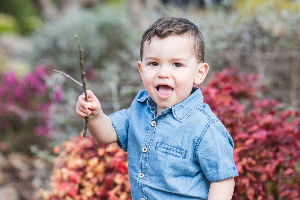 Mixed race aboriginal caucasian boy holding stick smiling with mouth open in garden - Australian Stock Image