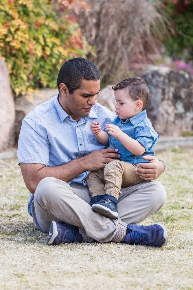 Mixed race aboriginal caucasian son sitting on dad's lap talking - Australian Stock Image