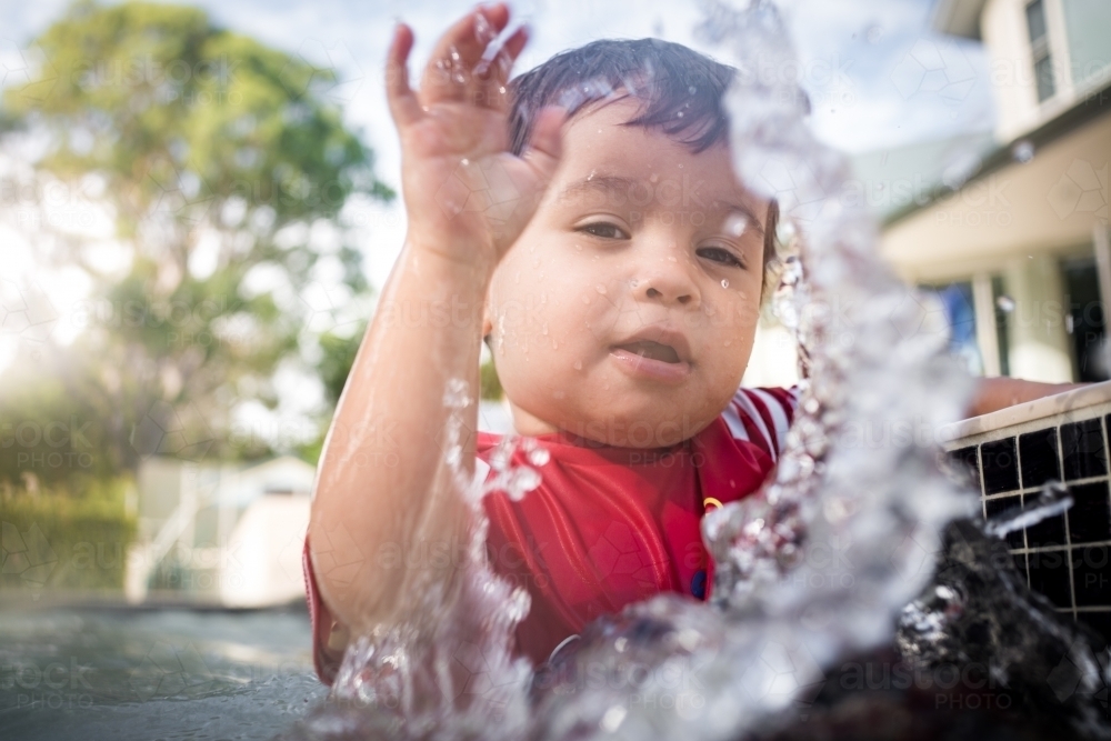 Mixed race baby boy swims and plays in a backyard pool - Australian Stock Image