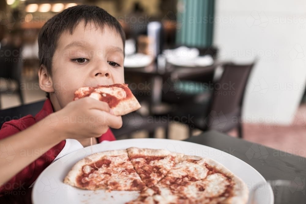 Mixed race boy eating pizza at a suburban Italian restaurant - Australian Stock Image