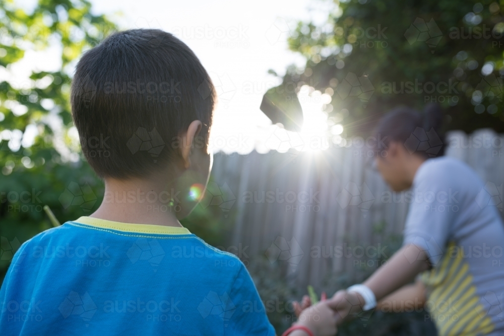 Mixed race boy helps his Asian mother harvest veggies from their backyard - Australian Stock Image