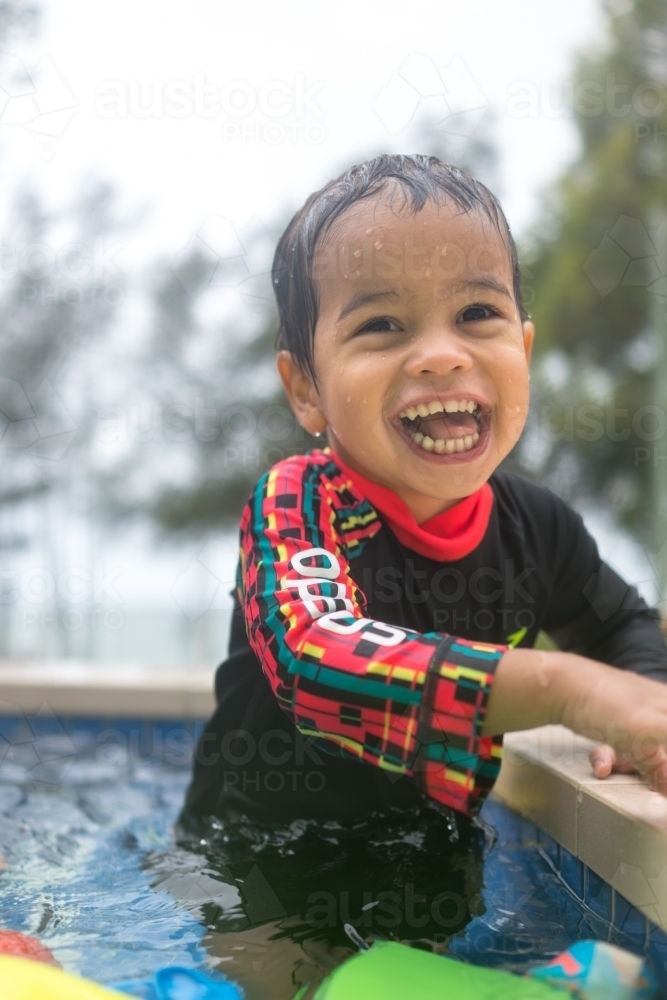 Mixed race boy playing in small backyard pool - Australian Stock Image