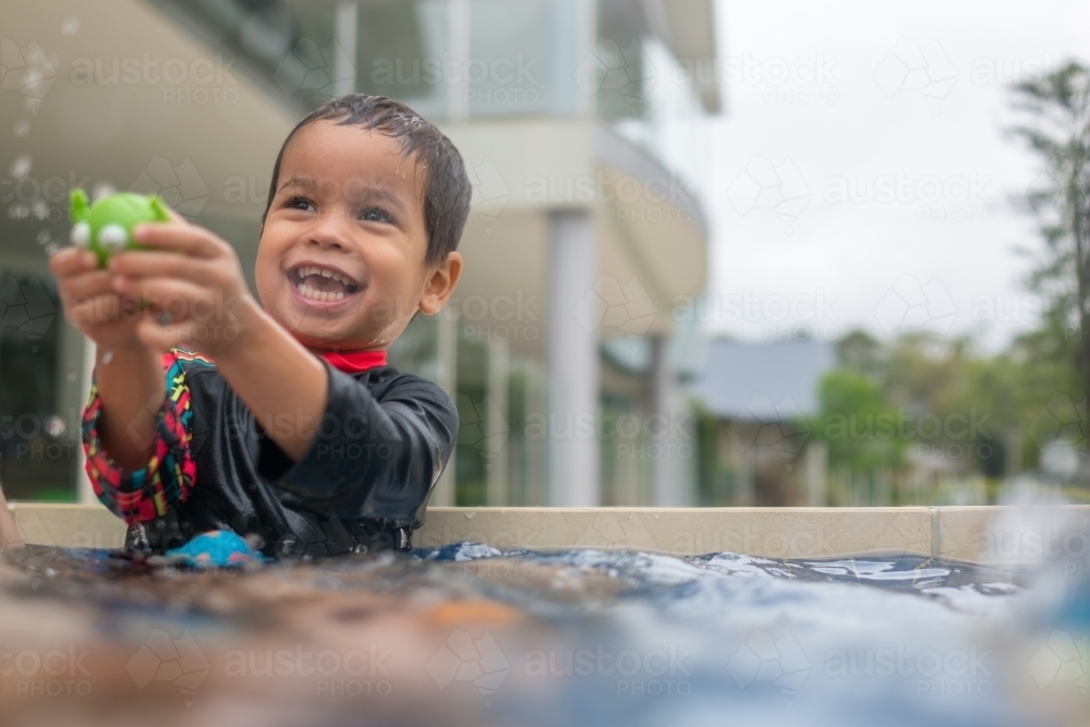 Mixed race boy playing in small backyard pool - Australian Stock Image