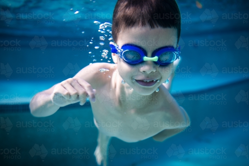 Mixed race boy swims and plays in a backyard pool - Australian Stock Image