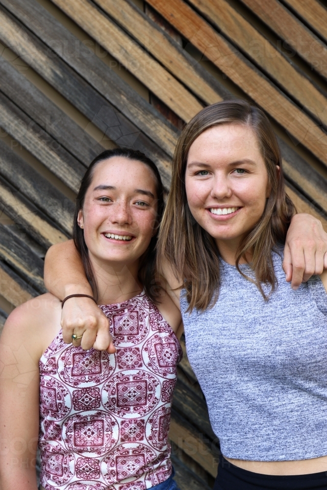 Mixed race sisters smiling in front of textured wooden paneling - Australian Stock Image