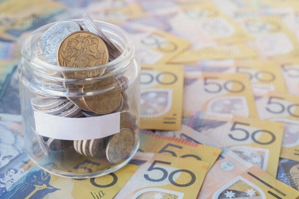 Money coins in jar on fifty dollar notes background - Australian Stock Image