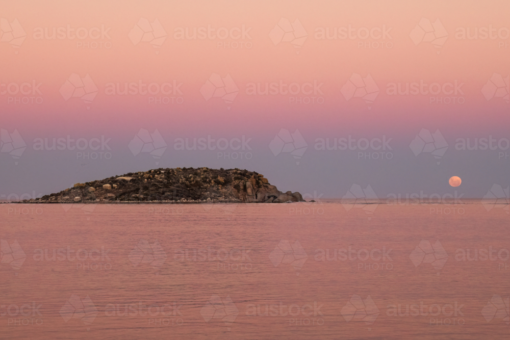 Moon going down over ocean with rocky island in foreground, Victor Harbor, South Australia - Australian Stock Image