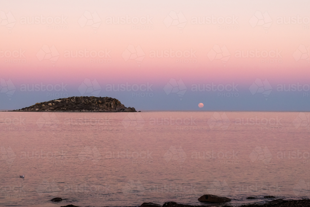 Moon going down over water with rocky island in foreground, Victor Harbor, South Australia - Australian Stock Image