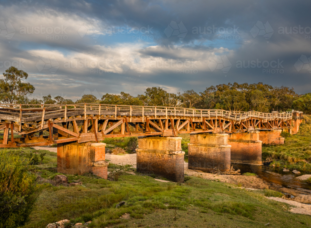 Morning sun on an old rickety railway bridge underneath a moody sky - Australian Stock Image