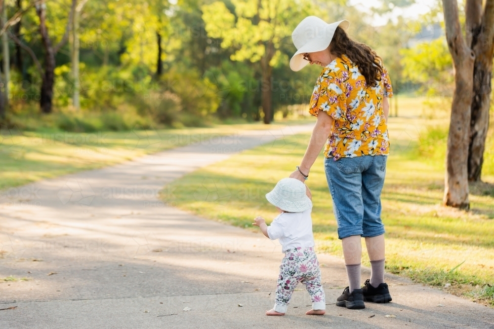 Mother and baby girl walking down footpath in parkland in Singleton - Australian Stock Image