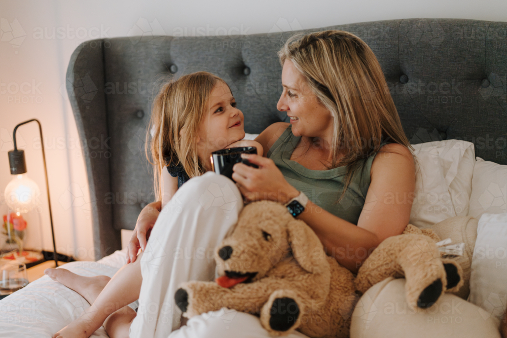 Mother and daughter cuddling on the bed with a stuffed animal. - Australian Stock Image