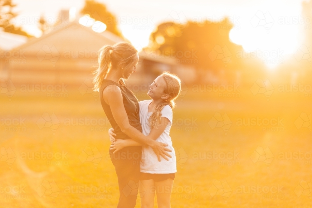 mother and daughter looking at each other and bathed in golden light with sun flare - Australian Stock Image