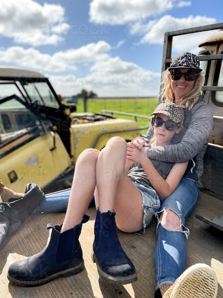 Mother and daughter sitting on old farm equipment embracing - Australian Stock Image