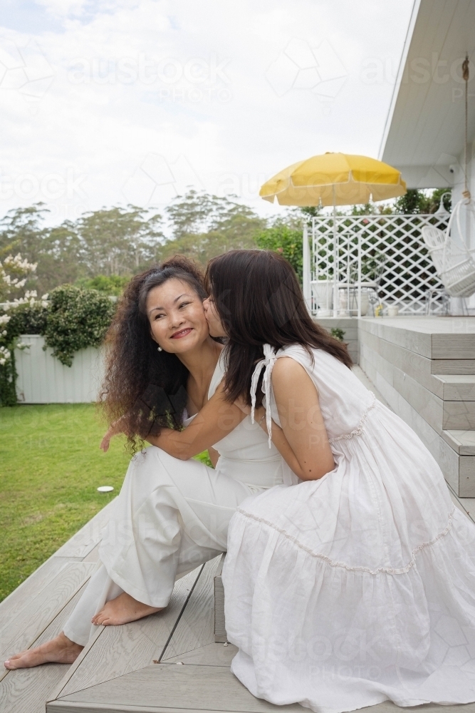 Mother and daughter sitting together on backyard steps - Australian Stock Image