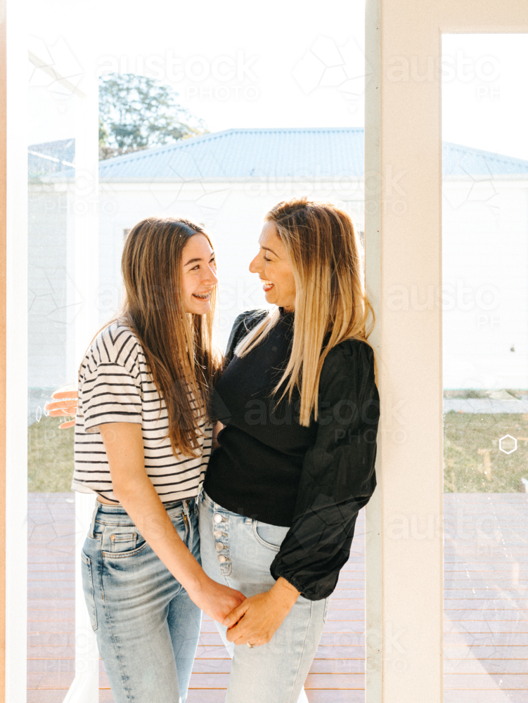 Mother and daughter standing in the doorway smiling while looking at each other. - Australian Stock Image