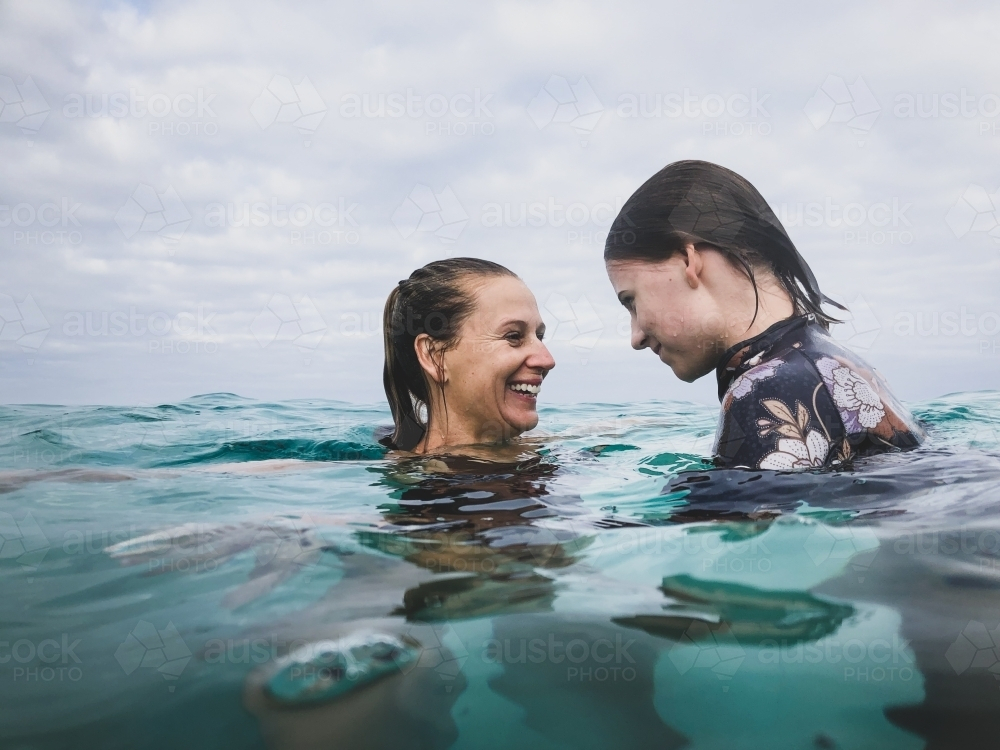 Mother and daughter swimming and playing, looking at each other in the ocean - Australian Stock Image