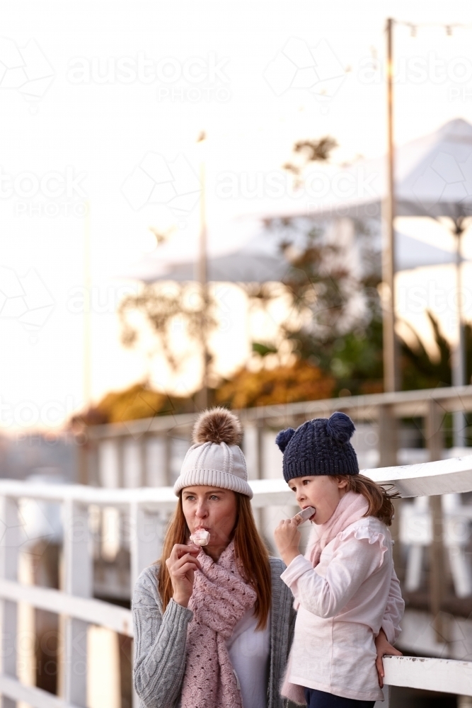 Mother and daughter wearing beanies on wharf eating ice creams - Australian Stock Image