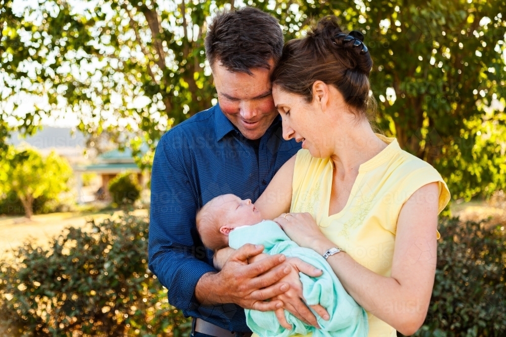 Mother and father cuddling with their baby in garden - Australian Stock Image