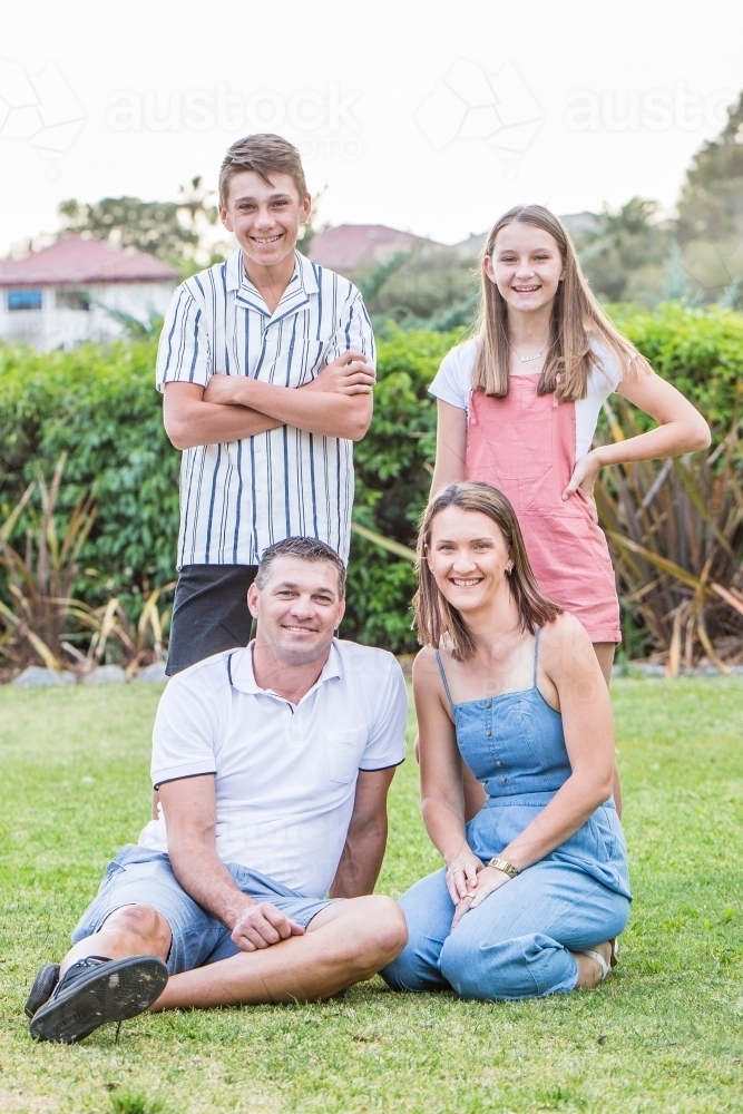 Mother and father sitting on grass while children stand above them - Australian Stock Image