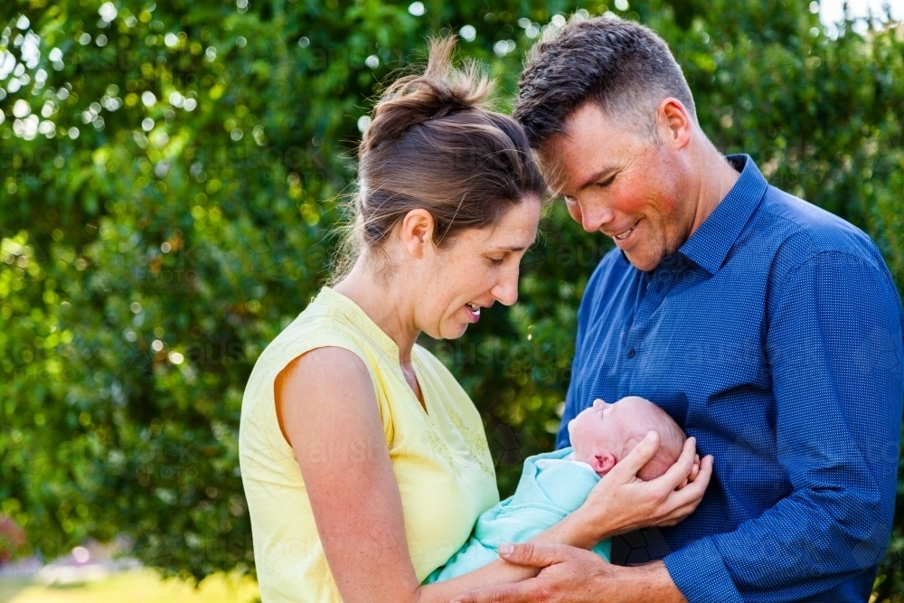 Mother and father smiling down at newborn child held in arms - Australian Stock Image