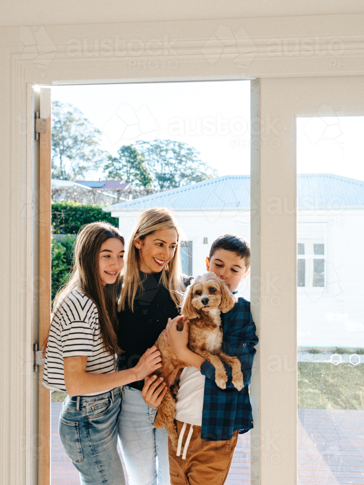 Mother and her kids holding a small dog in the doorway. - Australian Stock Image