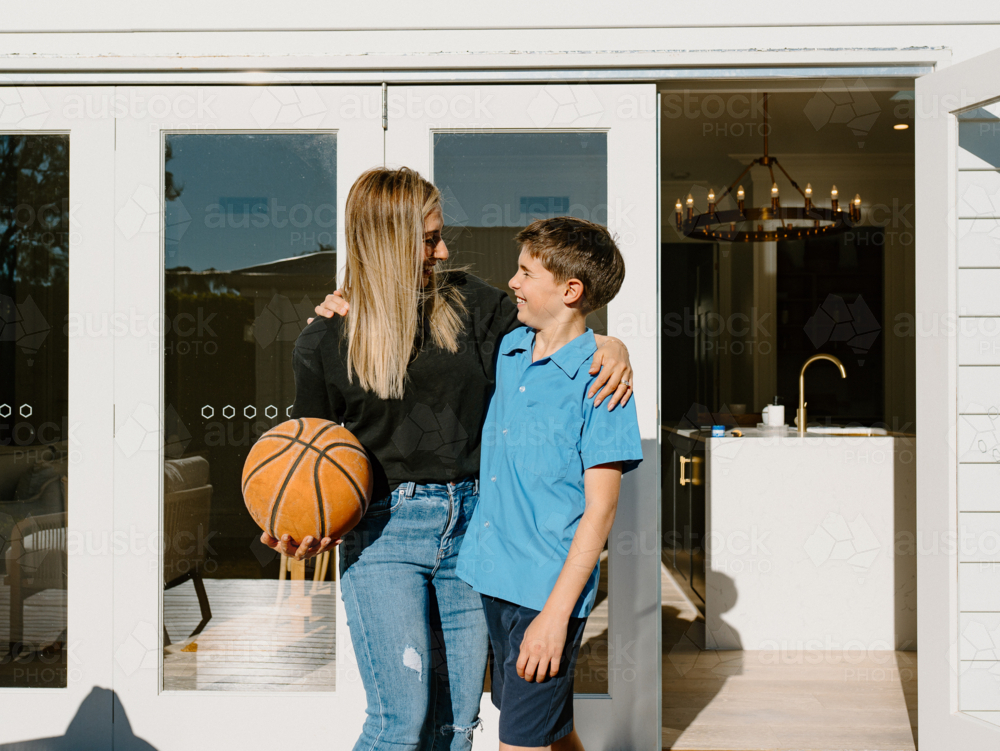 Mother and son looking at each other outside the house holding a basketball. - Australian Stock Image