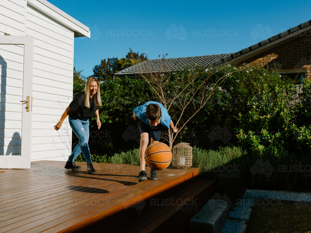 Mother and son playing basketball on the wooden deck. - Australian Stock Image