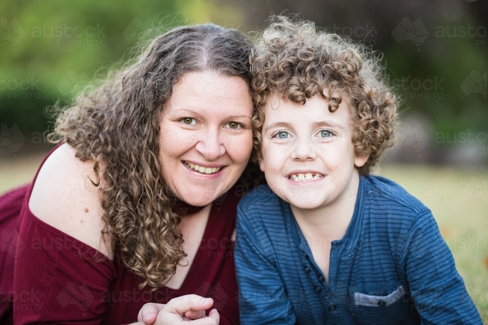 Mother and son with curly hair laying in garden smiling - Australian Stock Image