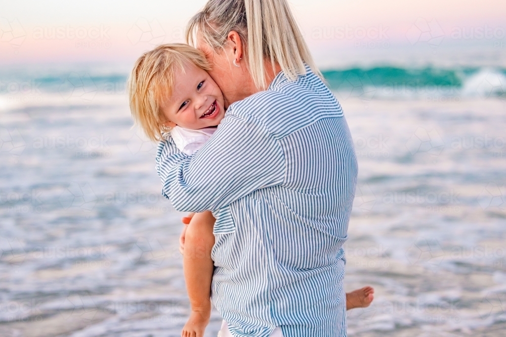 Mother and toddler son embracing on the beach with pink sunset sky - Australian Stock Image