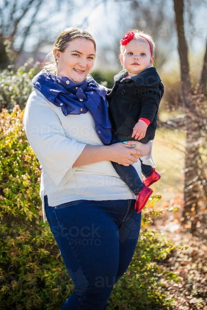 Mother holding baby girl on hip standing outside in garden - Australian Stock Image